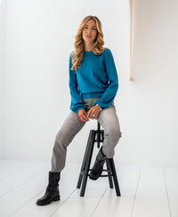 Blue merino wool sweater from PLEIN PUBLIQUE shown on a seated model in a minimalist setting.