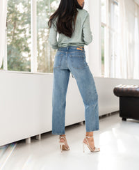 Woman stands indoors wearing light stone cropped jeans by windows.