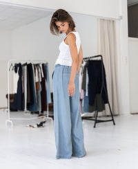 PLEIN PUBLIQUE Tencel jeans LE DEGAS in bleached color, shown worn by a woman standing by clothing racks.
