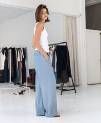 Woman wearing light-wash Tencel denim jeans stands by racks in a bright room.