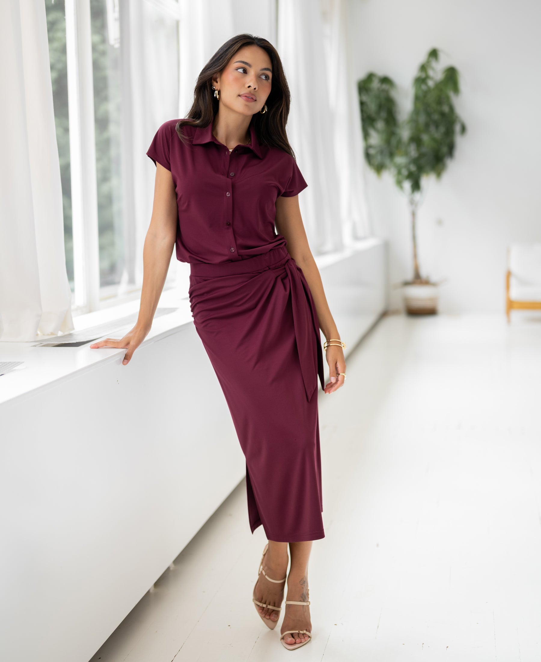 Travel skirt in wine red by PLEIN PUBLIQUE shown near a window in a bright, modern room.