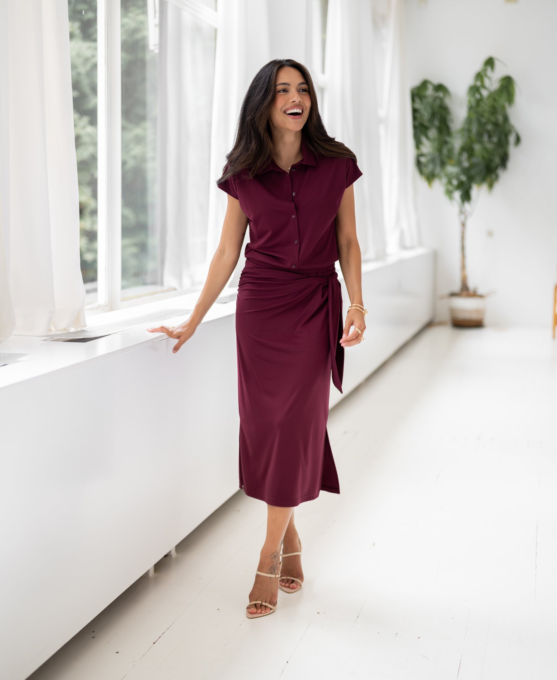 Burgundy LE MAEL travel skirt by PLEIN PUBLIQUE shown in a bright room with large windows.