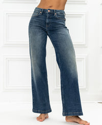 Wide leg blue vintage jeans by Plein Publique shown in front of a white paneled wall.