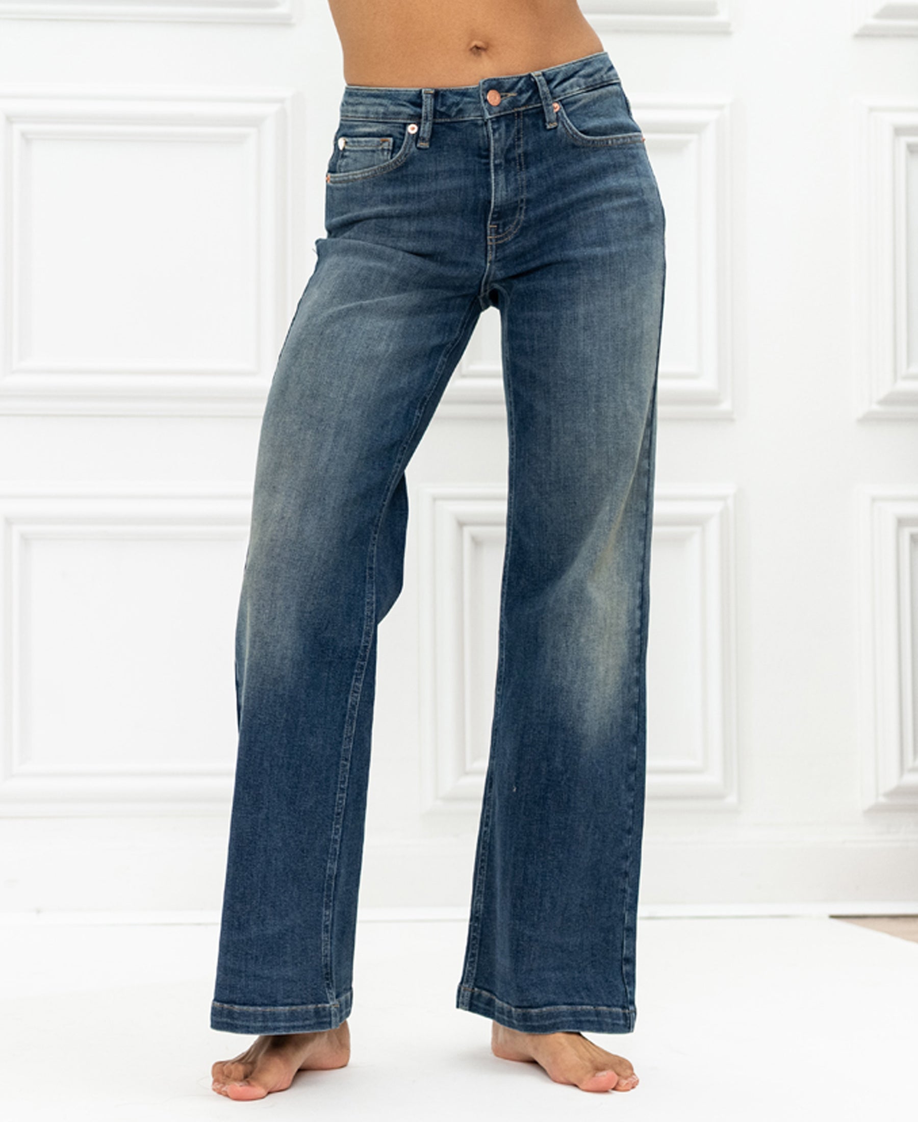 Blue vintage wide leg jeans by PLEIN PUBLIQUE LES DEUX against a white paneled wall.