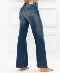 Wide leg jeans in blue vintage, shown from the back against a white paneled wall.