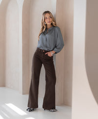 Brown wide leg jeans, shown on a woman standing by a cream arched wall, side view.