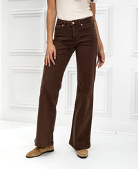 Person wearing PLEIN PUBLIQUE LES DEUX Cacao jeans stands by a white paneled wall.
