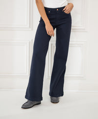 Person wearing Plein Publique Les Deux dark blue jeans against a white paneled wall.
