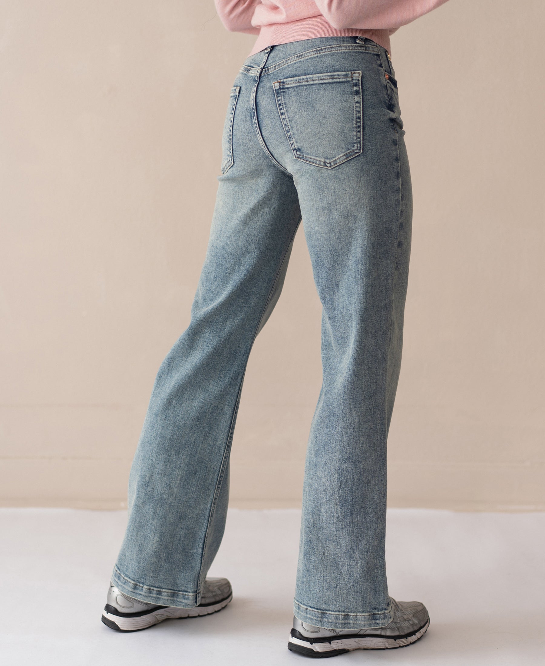 Person wearing wide leg vintage blue jeans, back to camera, against a neutral background.