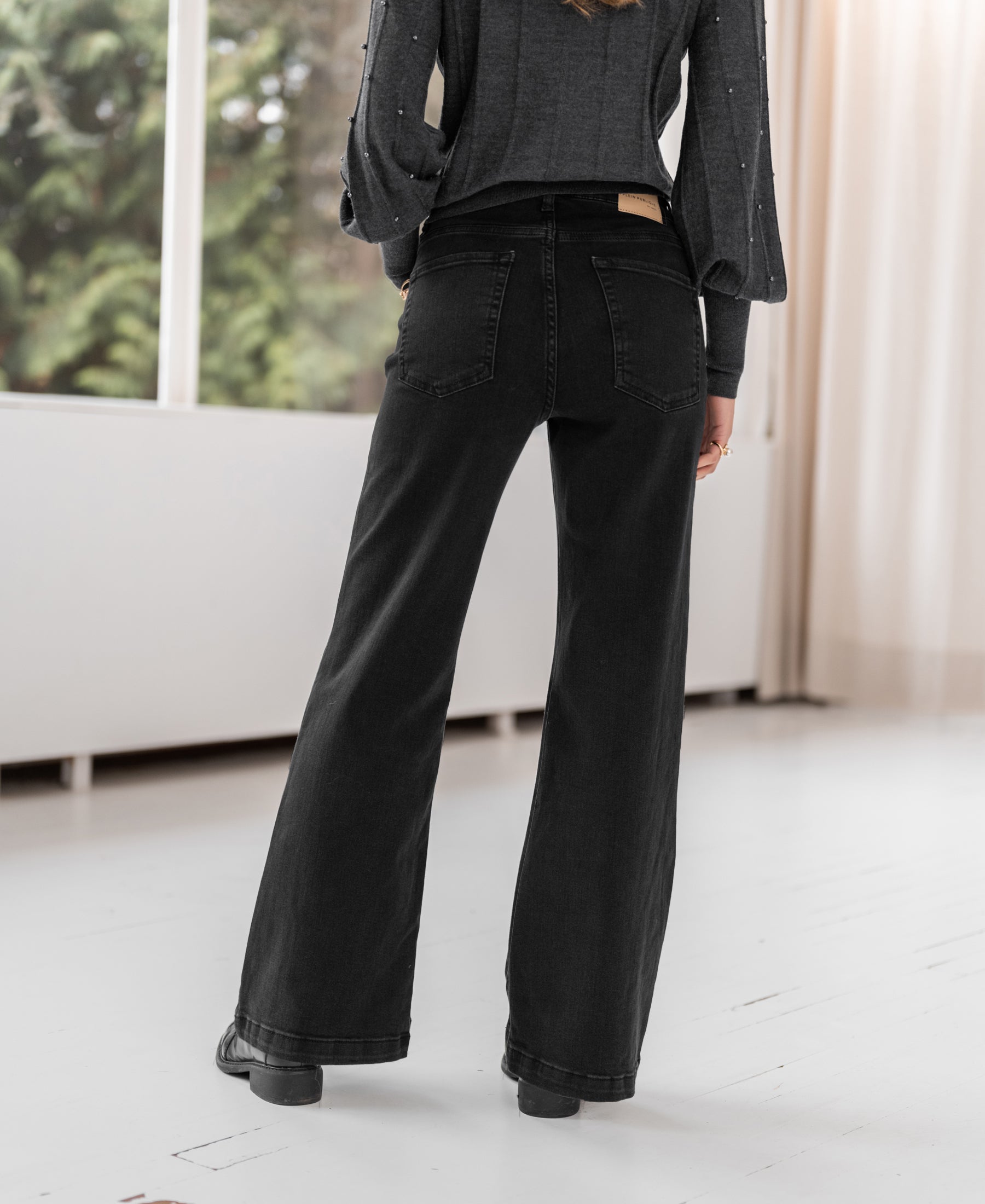Black denim wide leg jeans, back view, indoors.