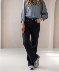 Woman wearing wide leg black denim jeans, standing indoors in a relaxed pose.