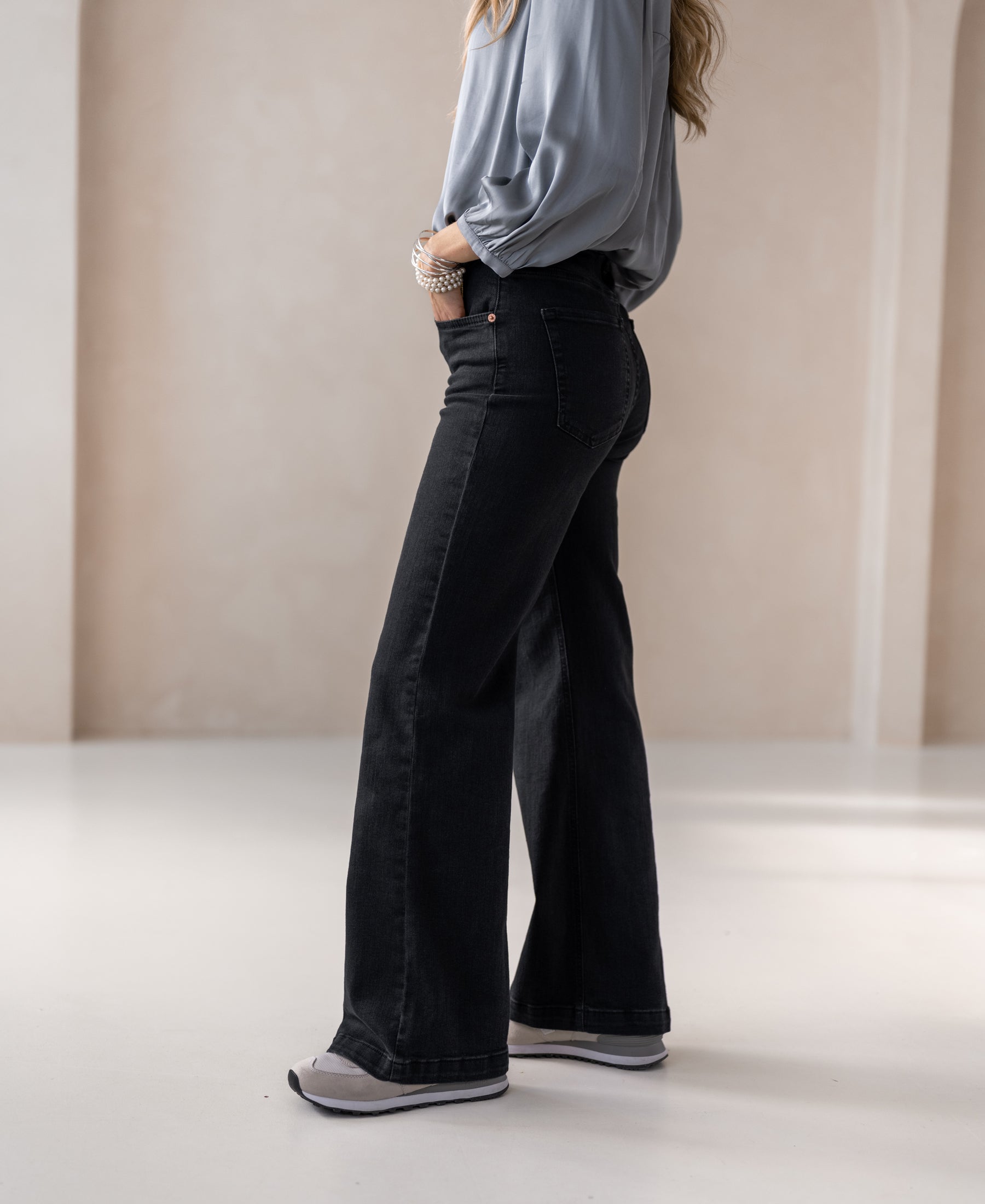 Woman facing away wearing wide-leg black denim jeans, hands in pockets.