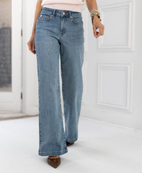 Wide leg jeans in light stone denim displayed indoors against a white wall.