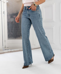 Wide leg jeans in light stone wash by PLEIN PUBLIQUE, shown near white paneled walls and a glass door.