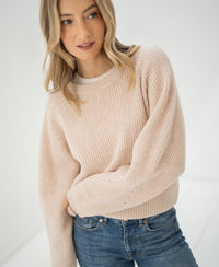 Woman wearing a LE DIJON Blush Merino wool sweater by PLEIN PUBLIQUE stands against a bright, minimal background.