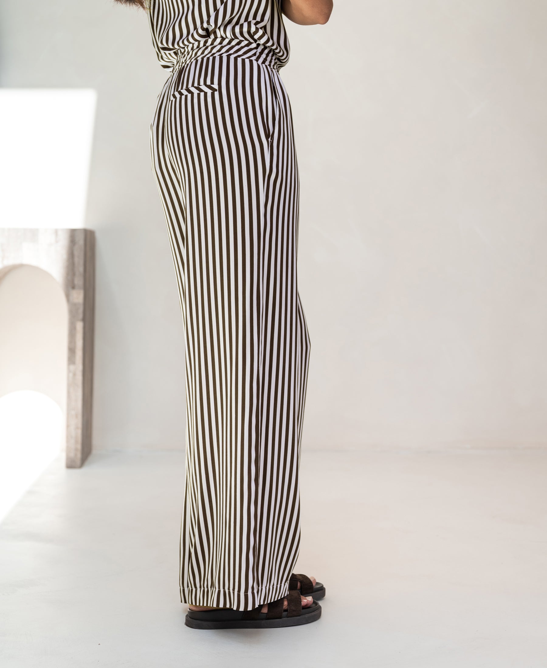 Ivory and cocoa striped summer pants in a minimal, bright room.