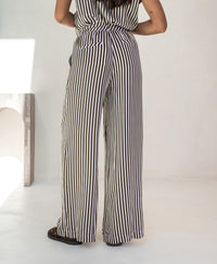 Woman wearing ivory-cocoa striped summer trousers, shown from the back, indoors.