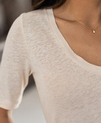 Close-up of a person wearing a cream linen T-shirt by PLEIN PUBLIQUE.
