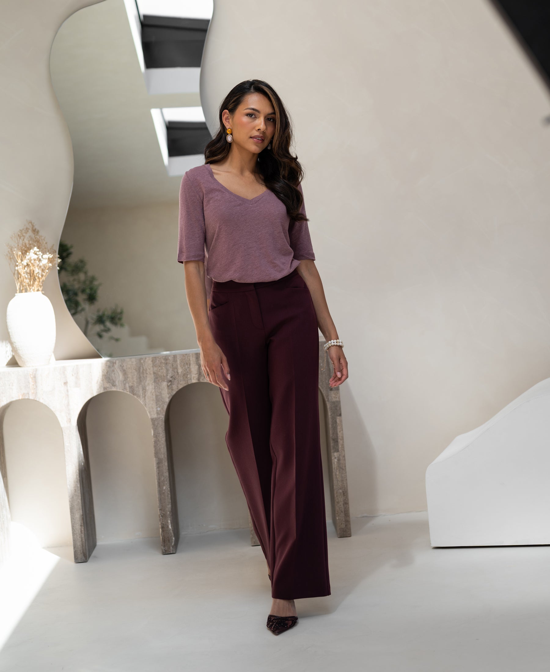 Woman wearing a mauve linen T-shirt by PLEIN PUBLIQUE stands indoors.