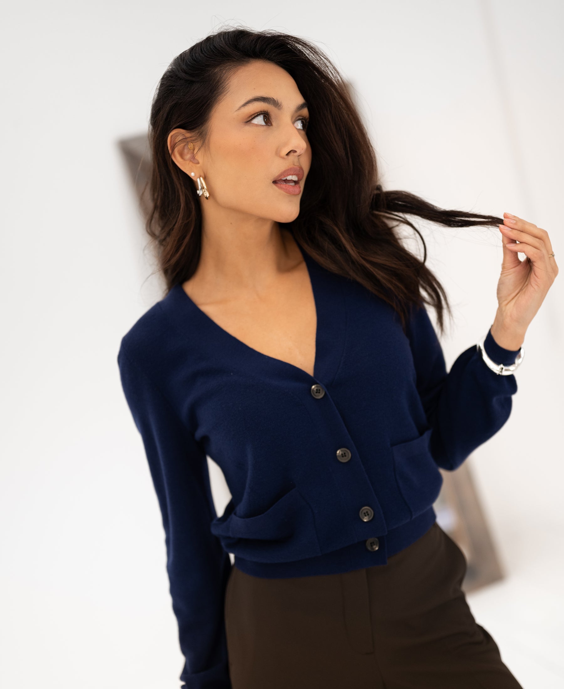 Woman wearing the Merino wool LA DONNA Navy cardigan by PLEIN PUBLIQUE, viewed from the side against a white background.