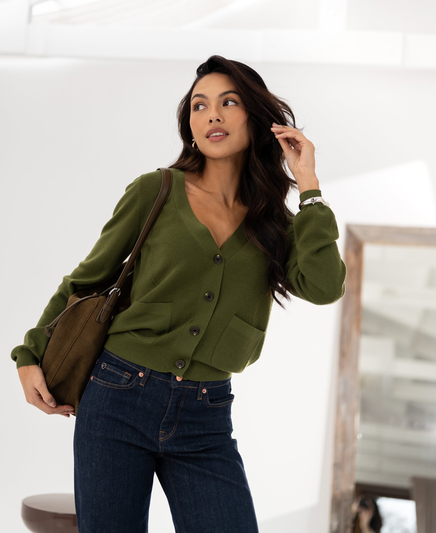 Vrouw met lang haar draagt het PLEIN PUBLIQUE Merino wool cardigan LA DONNA in olijfgroen bij een spiegel binnen.