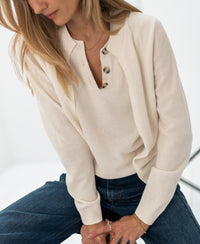 Ivory LA DOUBLE vest sweater by PLEIN PUBLIQUE, shown on model with hands folded, face partially out of frame.