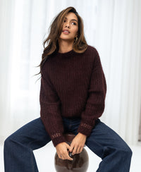 Woman wears the PLEIN PUBLIQUE Mohair sweater LA DOUCE in red-brown, seated on a stool looking upward.