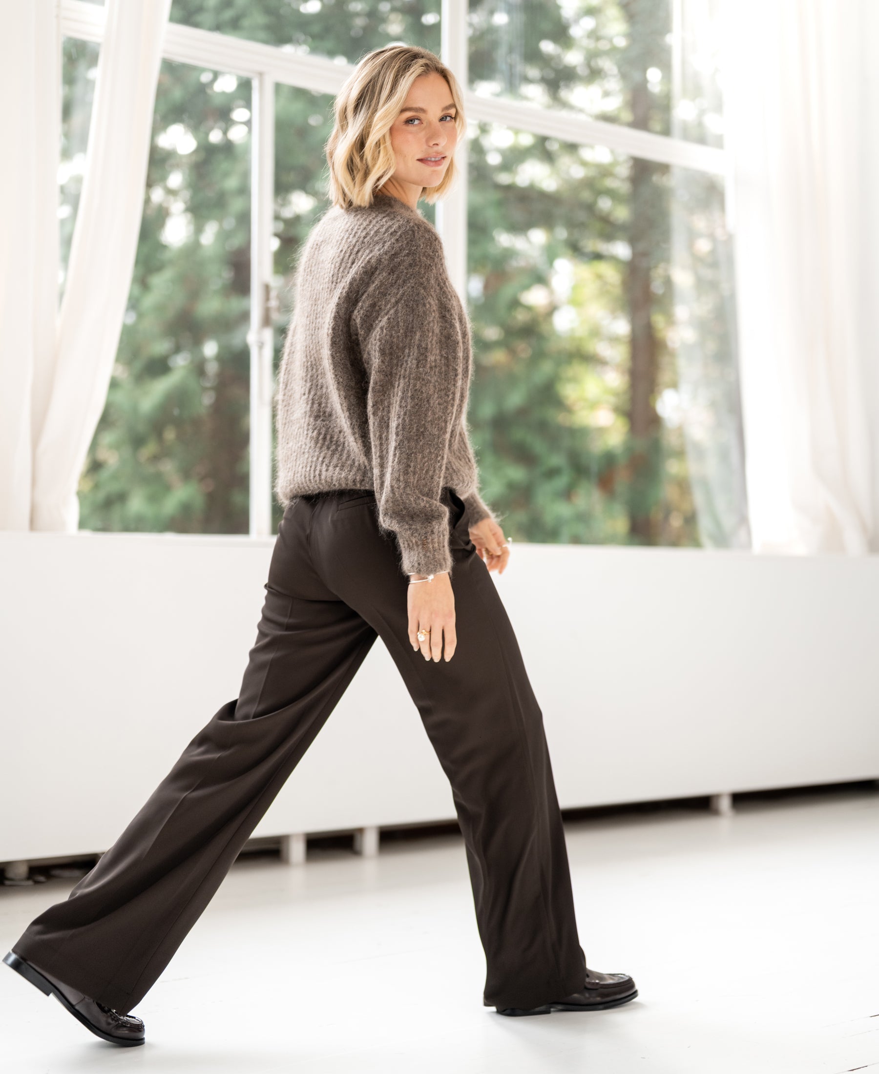 Semi-oversized light brown mohair sweater by PLEIN PUBLIQUE, shown indoors with greenery in the background.