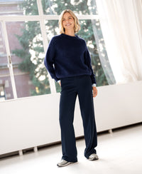 Woman wearing a PLEIN PUBLIQUE navy mohair sweater LA DOUCE, standing near large windows.