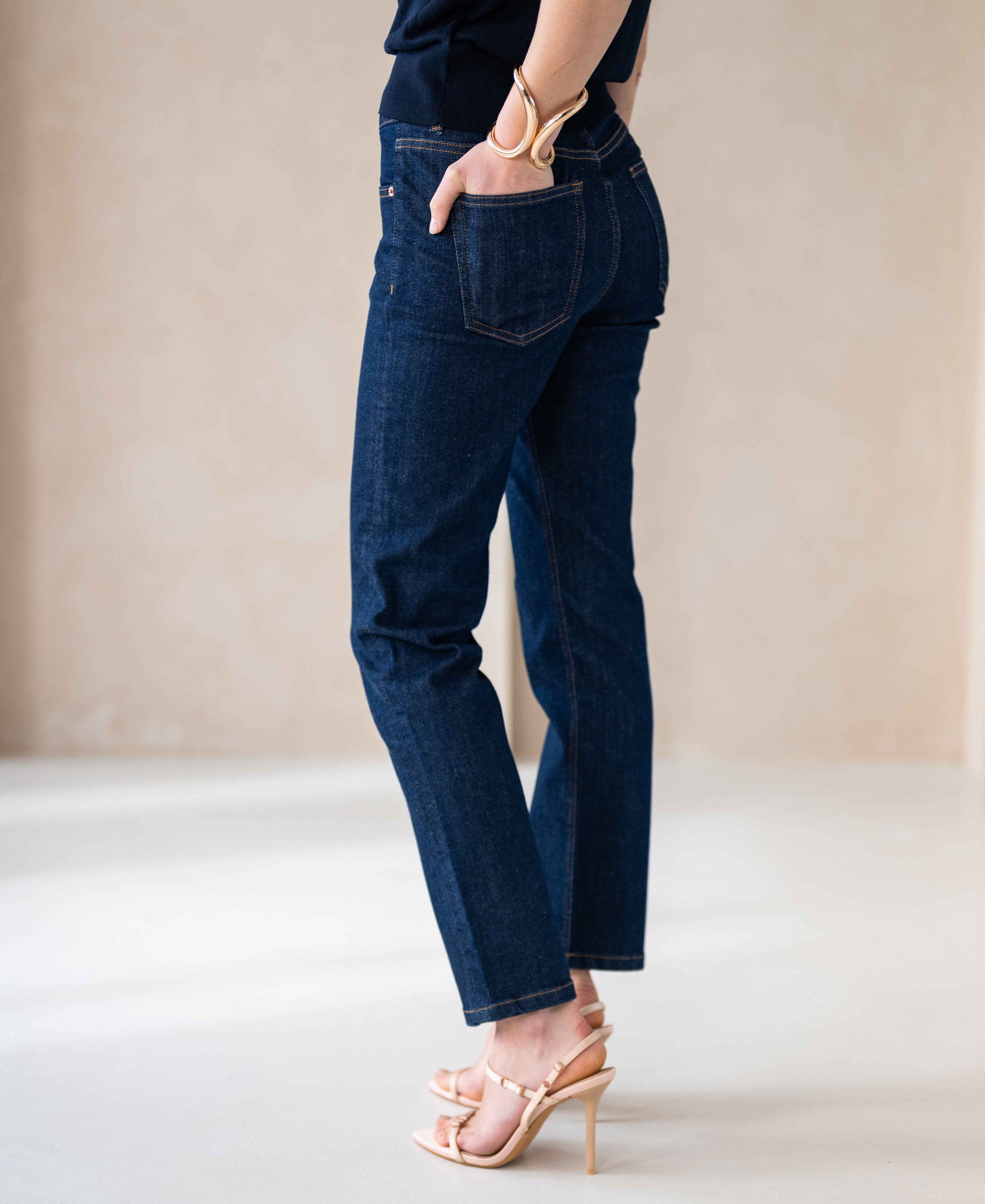 Person wearing dark blue cropped jeans, shown sideways with hand in pocket.