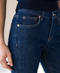 Waist-down view of person wearing dark blue cropped jeans in stretch denim, rinse-wash finish.