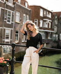 Woman wearing a black LA DOMI linen T-shirt by PLEIN PUBLIQUE, standing outdoors.