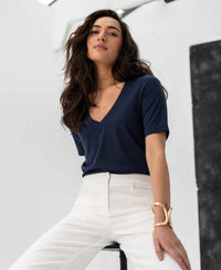 Woman wearing a PLEIN PUBLIQUE LA VERONIQUE V-neck T-shirt in dark blue, seated on a stool.