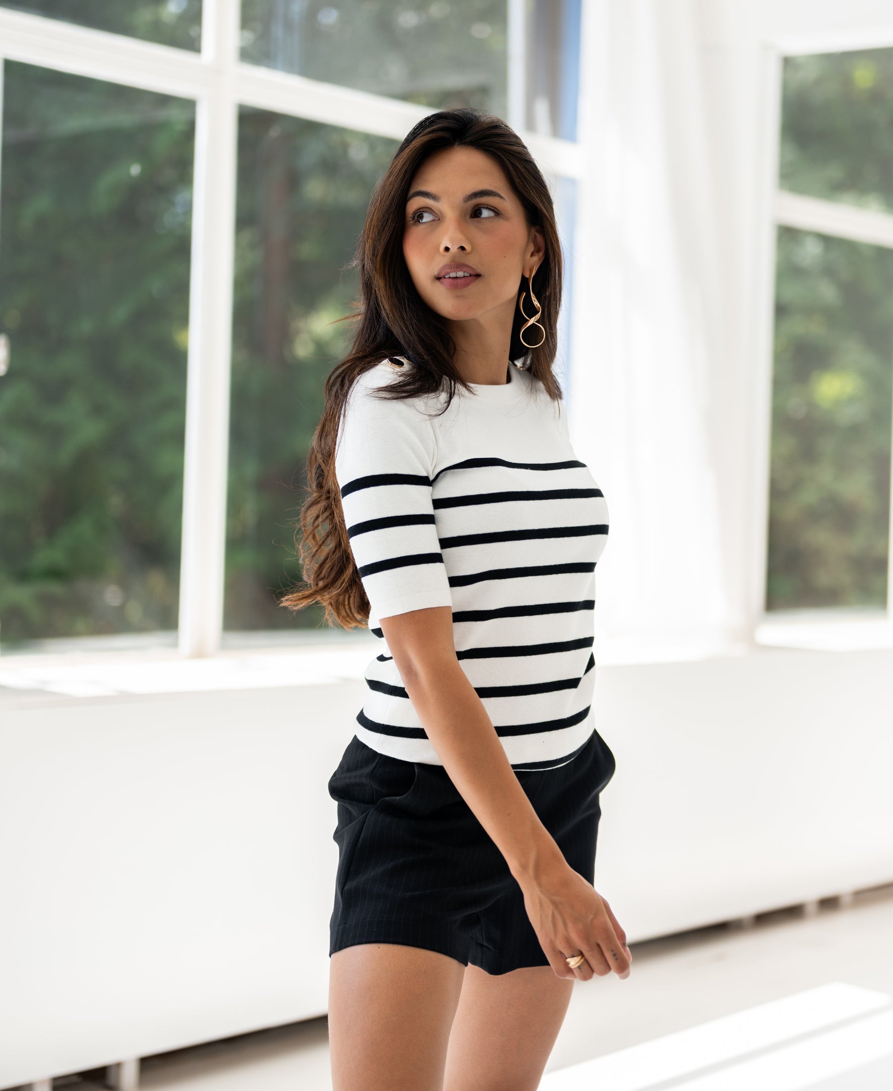 Breton striped sweater ESISA in ivory-black from PLEIN PUBLIQUE shown from the side by large sunny windows.