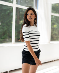 Breton striped sweater ESISA in ivory-black from PLEIN PUBLIQUE shown from the side by large sunny windows.