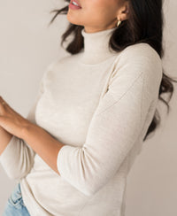 Beige turtleneck sweater in a ribbed knit, shown on a model against a neutral background.