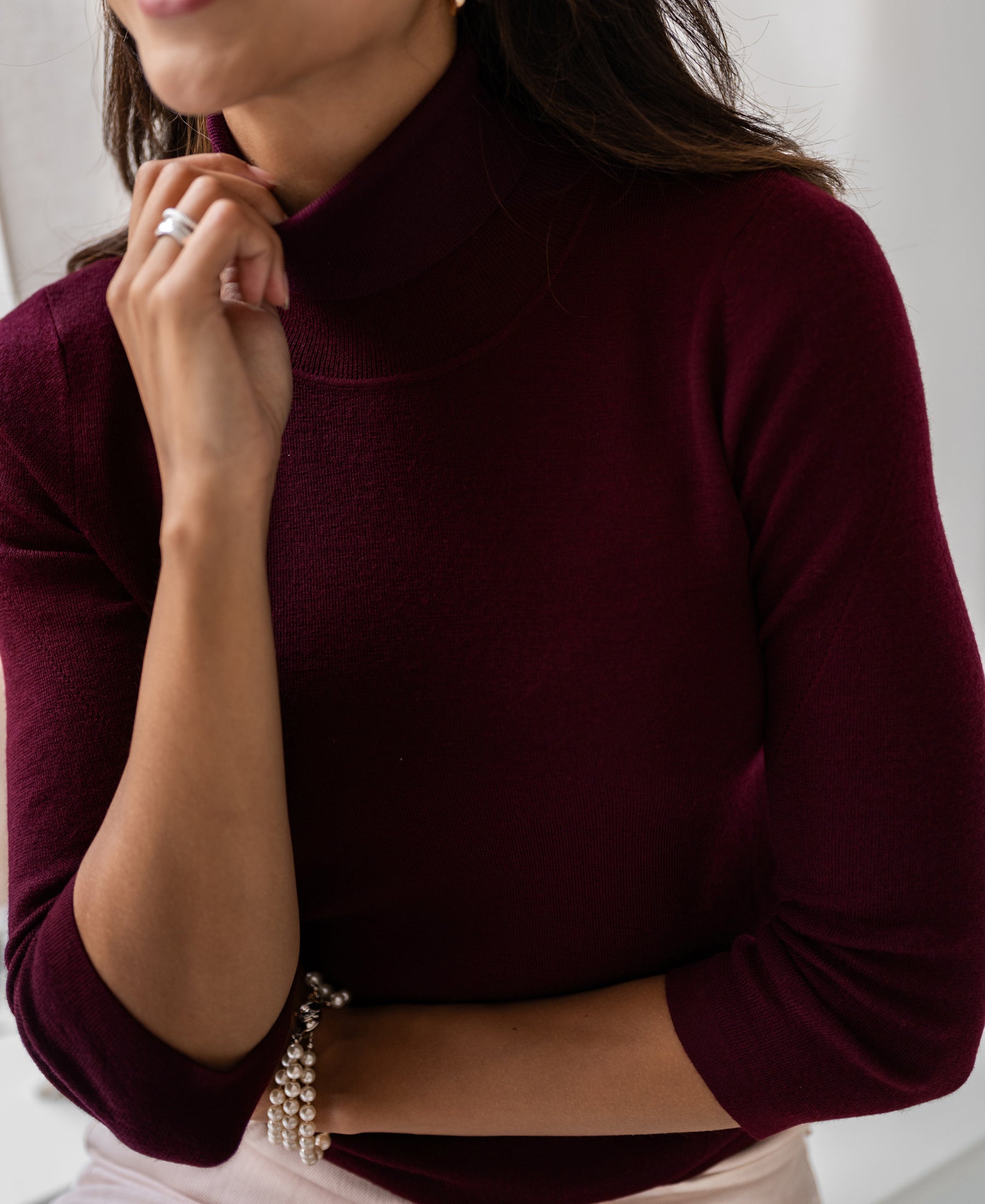 Woman wearing a Bordeaux turtleneck sweater by PLEIN PUBLIQUE, hand resting near her chin.