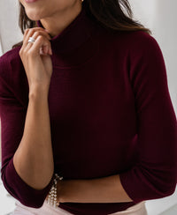 Woman wearing a Bordeaux turtleneck sweater by PLEIN PUBLIQUE, hand resting near her chin.