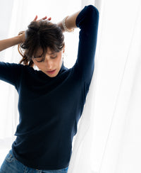 The LE FABIAN Dark Blue Turtleneck by PLEIN PUBLIQUE shown worn, with white curtains in the background.