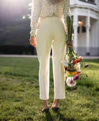 Cream cropped pants shown on a woman standing on grass near a white building.