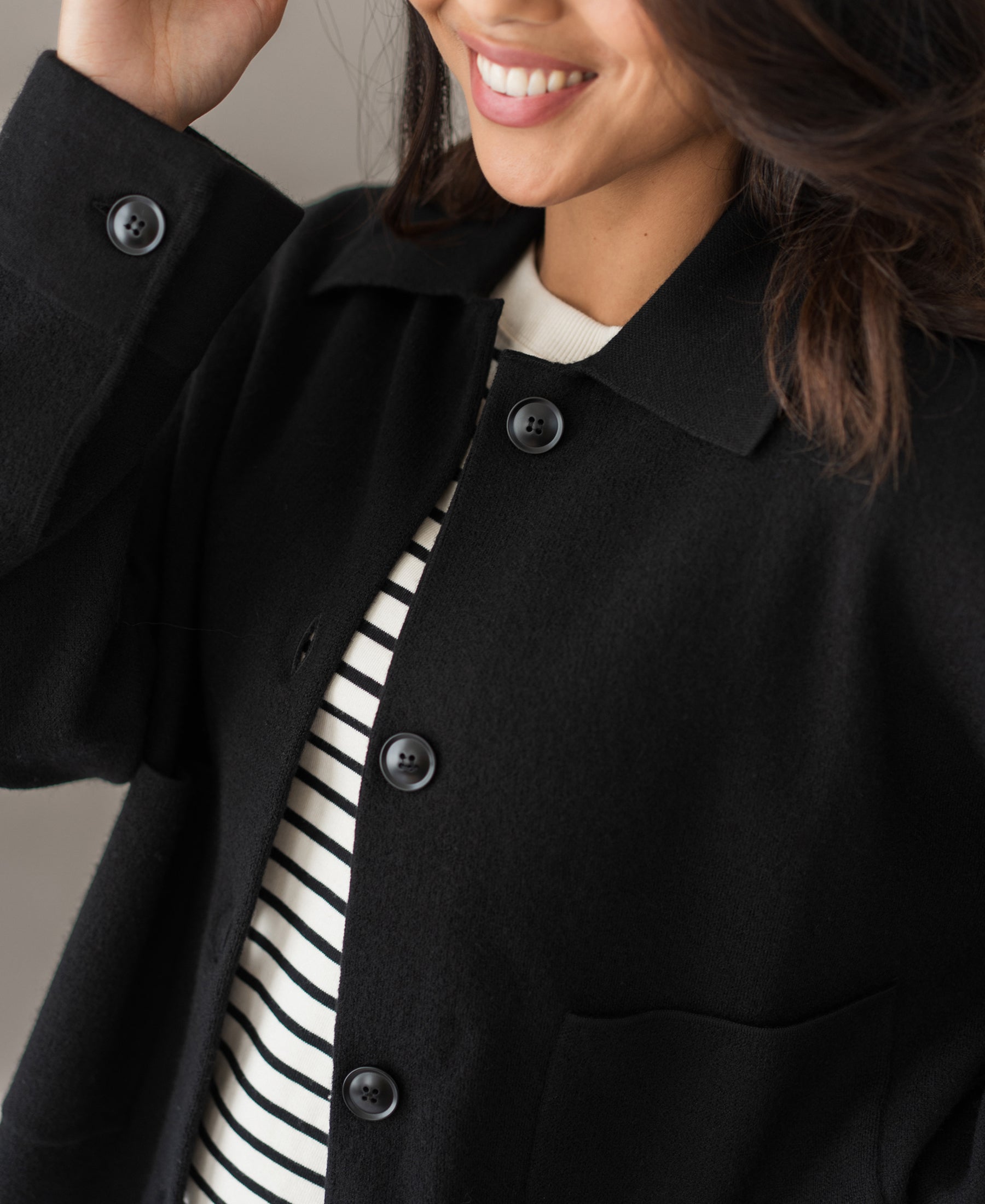 Woman wearing the LA FAYE black wool jacket, smiling with hand in hair.