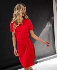 Red PLEIN PUBLIQUE LA FEE button dress shown against a dark, minimalist background.