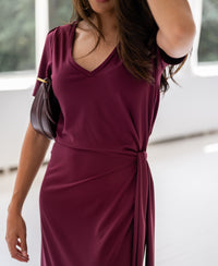 Woman wearing a wine-colored PLEIN PUBLIQUE long dress with v-neck, indoors.