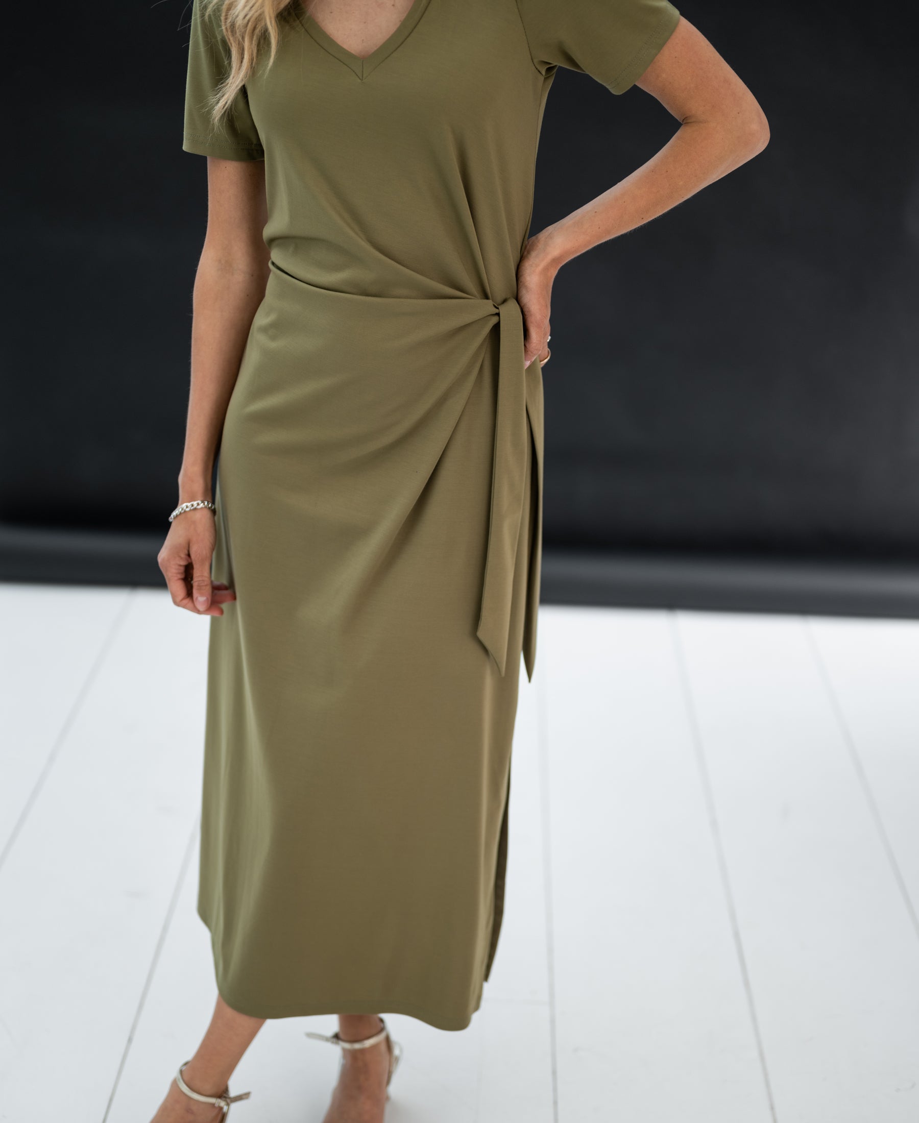 Long dress LA FILICIA in olive green, faux wrap midi style with side tie, displayed on a white floor.