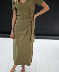 Long dress LA FILICIA in olive green, faux wrap midi style with side tie, displayed on a white floor.