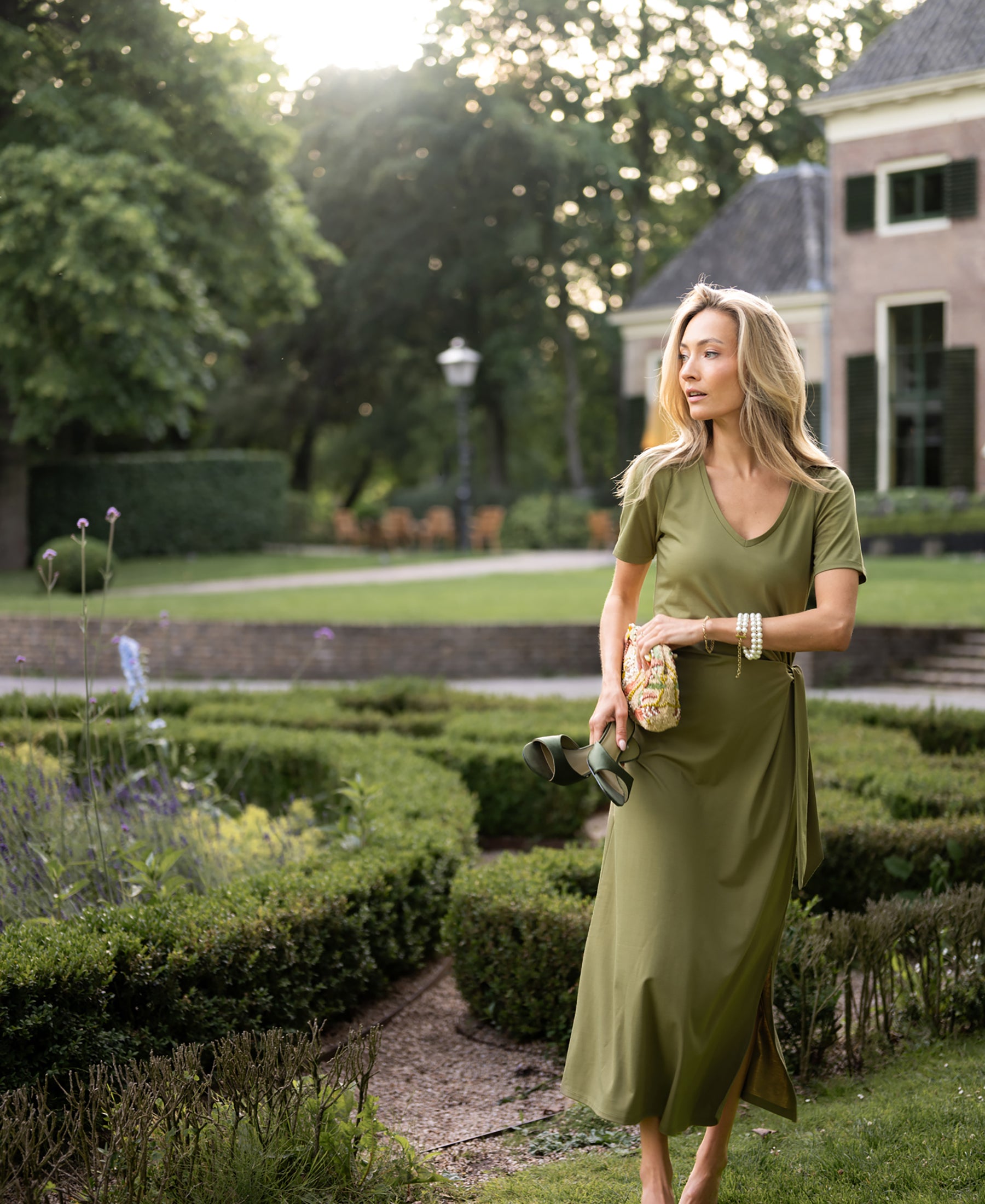 Olive green long dress by PLEIN PUBLIQUE LA FILICIA shown on woman walking in a garden.