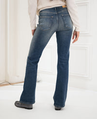 Person wearing blue vintage flared jeans by PLEIN PUBLIQUE, seen from behind indoors.