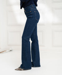 Model wearing dark wash flared jeans, standing sideways in a bright room.