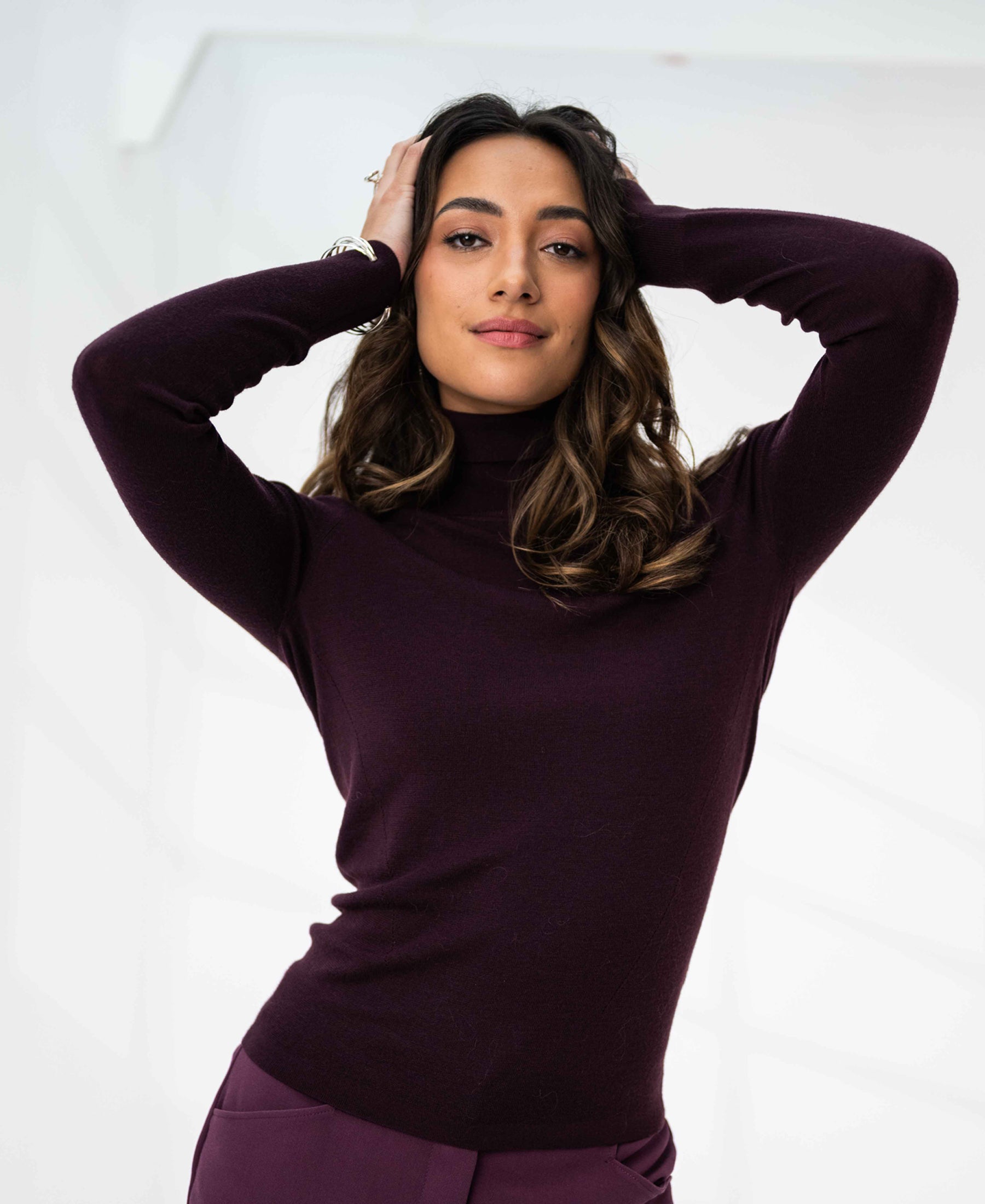 Woman wearing an aubergine Merino wool turtleneck sweater, shown against a white background.