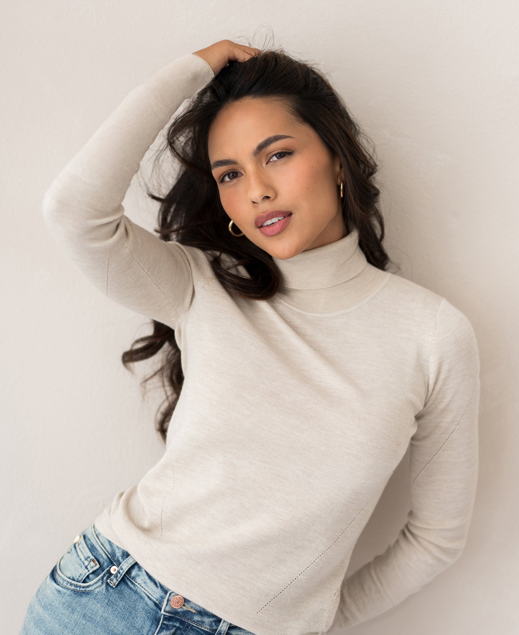 Beige merino wool turtleneck sweater shown on woman, PLEIN PUBLIQUE LA FORTE style, front view against light wall.